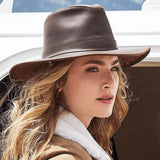 A lifestyle photo featuring a cowgirl wearing The Outrider - Brown Western Leather Aussie Hat. The hat showcases a classic Aussie cowboy hat style with its brown leather construction and wide brim. The cowgirl exudes confidence and embodies the adventurous spirit of the Wild West.