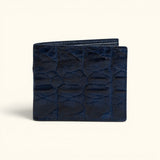 The Monarch Crocodile Bifold Wallet in Deep Midnight Blue featuring genuine crocodile leather with a symmetrical scale pattern and slim bifold design, shown in a front view on a soft ivory background.