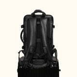 The Stetson Peak - Expandable Men's Leather Backpack in black, back view showing the backpack secured on top of a trolley, highlighting its travel-friendly design with padded shoulder straps and ergonomic support.