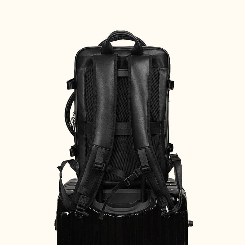 The Stetson Peak - Expandable Men's Leather Backpack in black, back view showing the backpack secured on top of a trolley, highlighting its travel-friendly design with padded shoulder straps and ergonomic support.