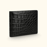 Angled view of The Ashford black Siamese crocodile bifold wallet, highlighting its continuous full-belly exterior, natural scale pattern, and slim luxury profile.