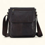 Front view of The Dustwalker full-grain cow leather crossbody iPad bag in coffee brown with flap cover, front stitching, and adjustable strap.