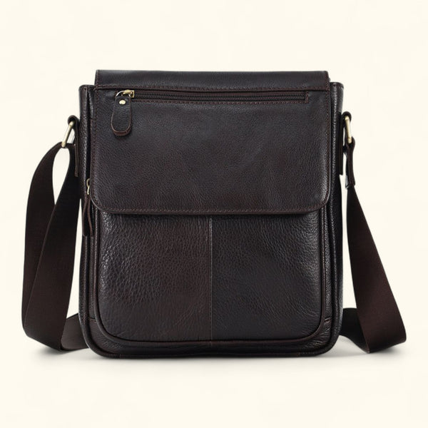 Front view of The Dustwalker full-grain cow leather crossbody iPad bag in coffee brown with flap cover, front stitching, and adjustable strap.