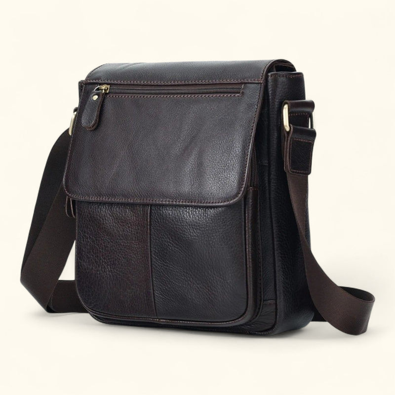 Angled side view of The Dustwalker full-grain cow leather crossbody iPad bag in coffee brown with adjustable strap and front flap design.