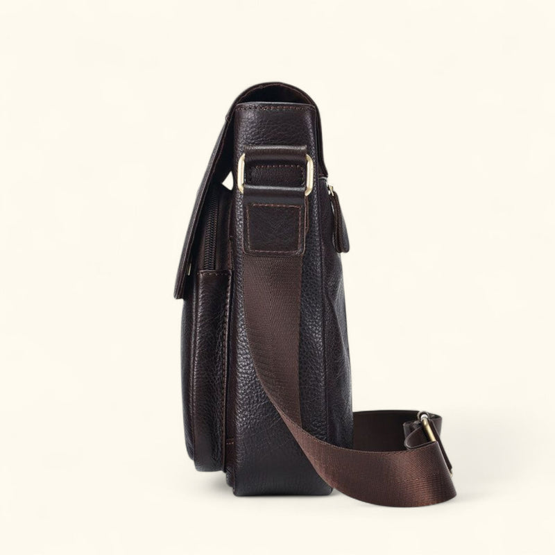 Side profile view of The Dustwalker full-grain cow leather crossbody iPad bag in coffee brown with adjustable strap and reinforced brass hardware.