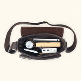 Top view of The Dustwalker full-grain cow leather crossbody iPad bag packed with watch, smartphone, power bank, notebook, and accessories inside.