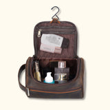 The High Plains Leather Toiletry Bag opened to reveal its spacious interior, featuring various toiletries and cosmetics neatly stored, with a hanging hook for convenience and mesh zippered pockets for organization.