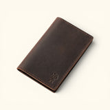 Angled view of The Rancher's Legacy brown Western cardholder wallet featuring an embossed cowboy logo, slim folded construction, and durable edge stitching.