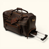 The Lawful Leather Duffle with Wheels shown in a three quarter angle with the telescoping handle extended, featuring premium full grain leather, smooth rolling wheels, a front organizer pocket, and durable travel construction.