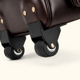 Close up of The Lawful Leather Duffle with Wheels featuring smooth rolling spinner wheels, reinforced wheel housing, premium leather construction, and durable travel ready hardware.