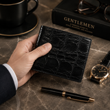 Lifestyle image of The Monarch Crocodile Bifold Wallet in Obsidian Black genuine Siamese crocodile leather displayed in hand on a luxury desk setting.