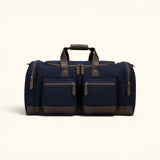 The Weekender navy waxed canvas duffel bag with brown leather trim, multiple zippered pockets, and reinforced carry handles.