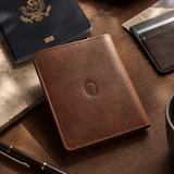 The Western Traveler brown leather passport holder on a wooden desk with a passport, pen, and travel essentials.