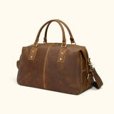 Angled view of The Wolf brown leather overnight travel bag with a detachable shoulder strap, durable carry handles, and rugged vintage finish.