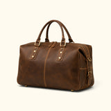 Hero angle view of The Wolf full-grain leather travel duffel featuring a rich brown finish, reinforced handles, dual zippers, and antique brass hardware.