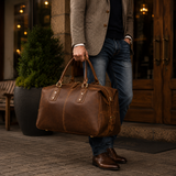 Man carrying The Wolf luxury men’s leather weekender bag, featuring full-grain brown leather, reinforced handles, and antique brass hardware.