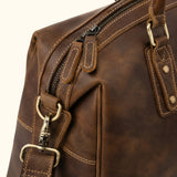 Close-up of The Wolf rugged leather duffel featuring dual zipper pulls, reinforced stitching, antique brass hardware, and a detachable shoulder strap attachment.