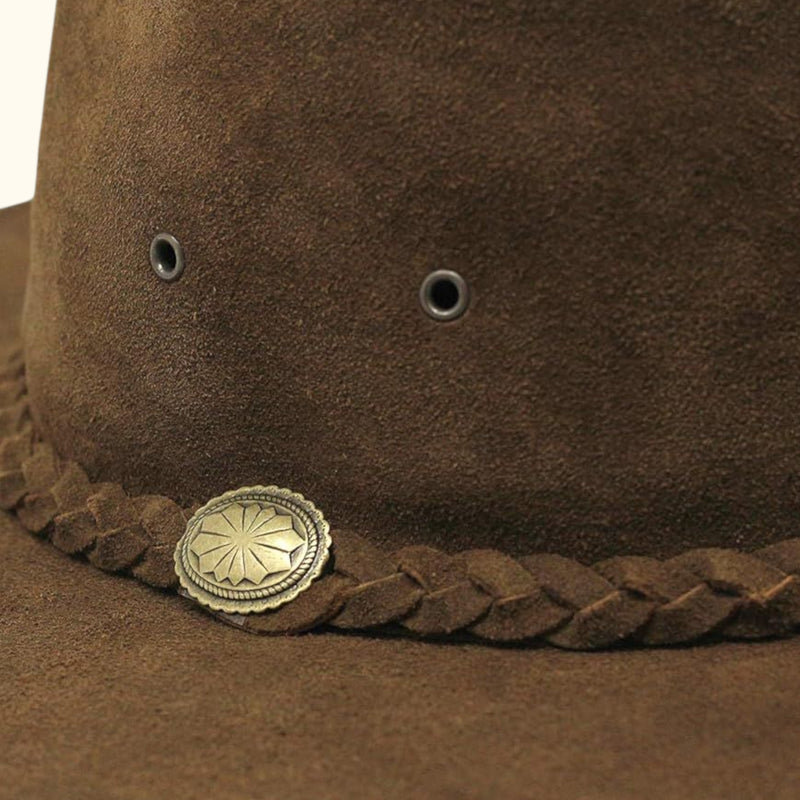 Close-up detail of The Trailsman – showing the brown suede texture, metal eyelets, braided hatband, and engraved concho.