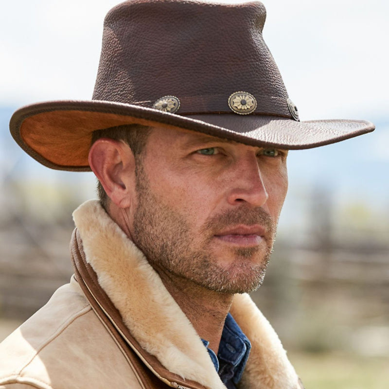 Man wearing the Walker full-grain leather western hat outdoors, showcasing concho band and curved brim in a rugged ranch setting